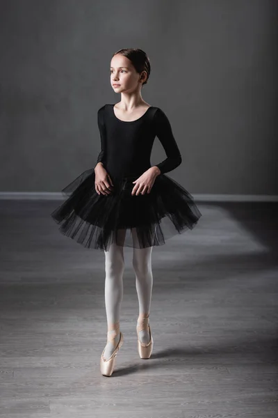 Preteen girl in black tutu and pointe shoes standing on toe while training in studio — Stock Photo