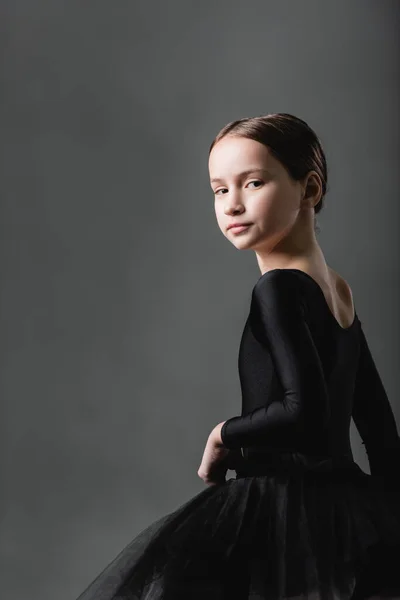 Menina graciosa em traje de balé preto olhando para a câmera no fundo cinza — Fotografia de Stock