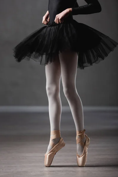 Cropped view of girl in black tutu and pointe shoes dancing in ballet studio — Stock Photo
