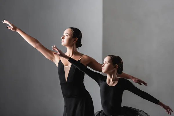 Elegante maestro de ballet y niña bailando sobre fondo gris - foto de stock