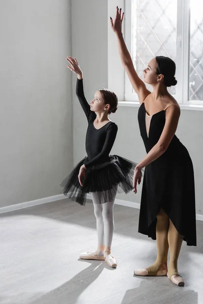 Visão de comprimento total da menina aprendendo a dançar balé perto de bailarina graciosa — Fotografia de Stock