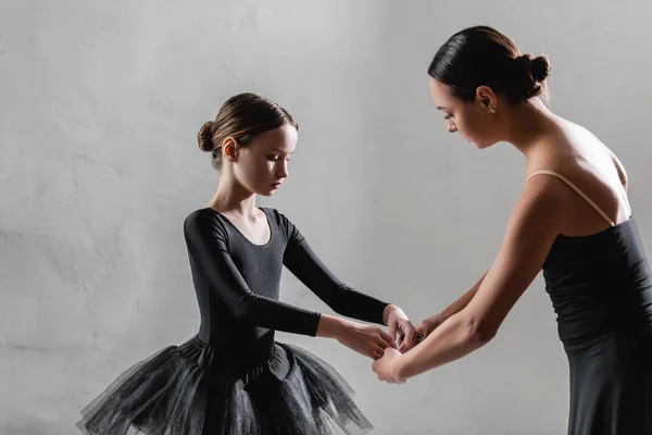 Учитель балета показывает хореографический элемент девушке в черной пачке на сером фоне — стоковое фото