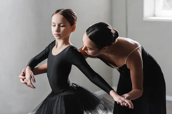 Young ballet teacher assisting girl in black tutu during dance lesson — Stock Photo