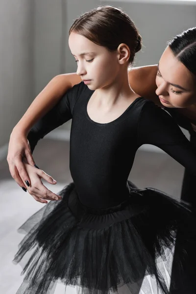 Profesora de ballet cogida de la mano de chica en tutú negro durante la lección de baile - foto de stock