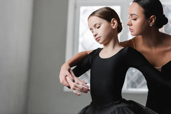 Молодая балерина помогает девушке научиться танцевать балет — стоковое фото