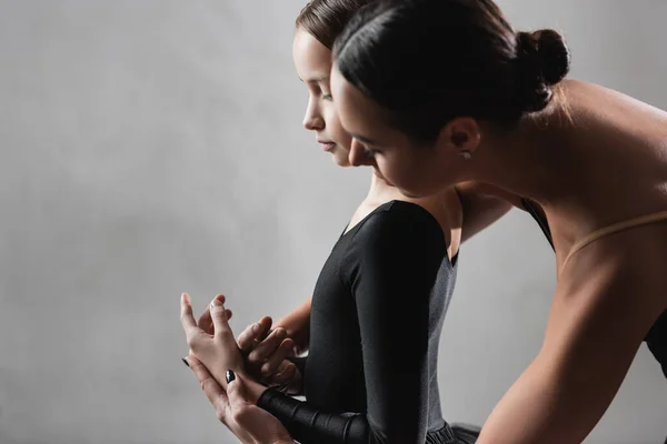 Vista laterale del maestro di balletto insegnare ragazza a ballare su sfondo grigio — Foto stock