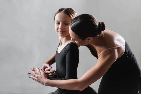 Jovem professor de balé tocando as mãos da menina durante a aula de dança em fundo cinza — Fotografia de Stock