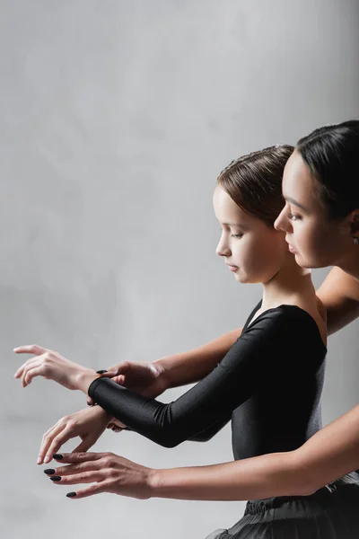 Вид сбоку преподавателя танцев, показывающего девочке элементы балет на сером фоне — стоковое фото