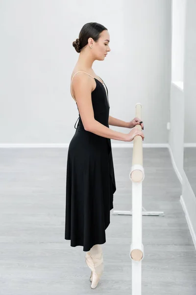 Side view of ballet dancer in pointe shoes standing on toe at barre in studio — Stock Photo