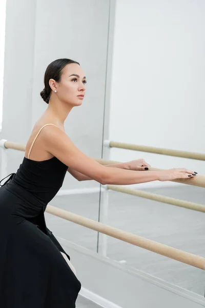 Jovem bailarina em vestido preto olhando para longe durante o exercício no estúdio — Fotografia de Stock