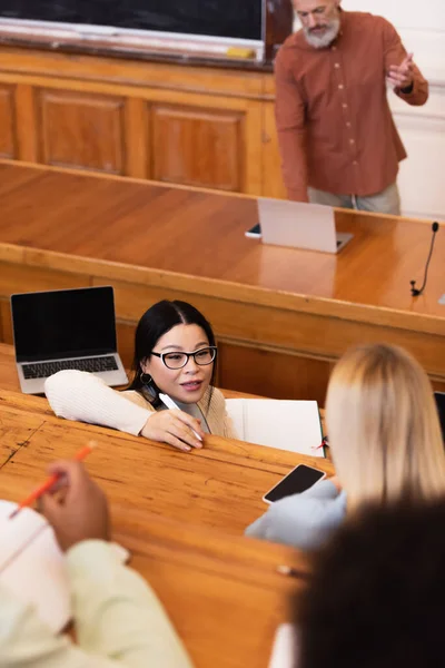 Asian student talking to friend near devices in university — Stock Photo