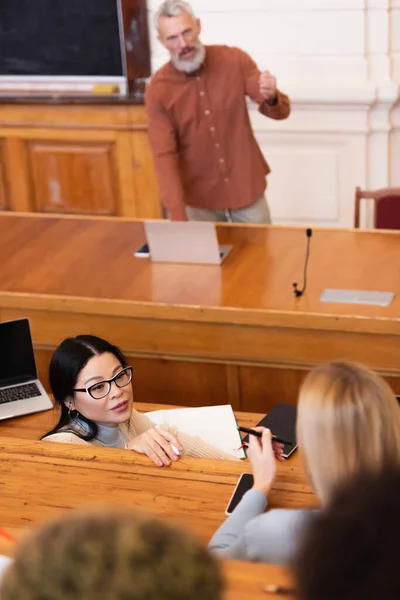 Estudante asiático conversando com amigo perto de dispositivos e cadernos na universidade — Fotografia de Stock