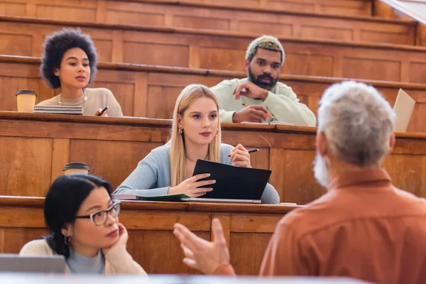 Estudantes multiculturais olhando para professor desfocado no auditório universitário — Fotografia de Stock