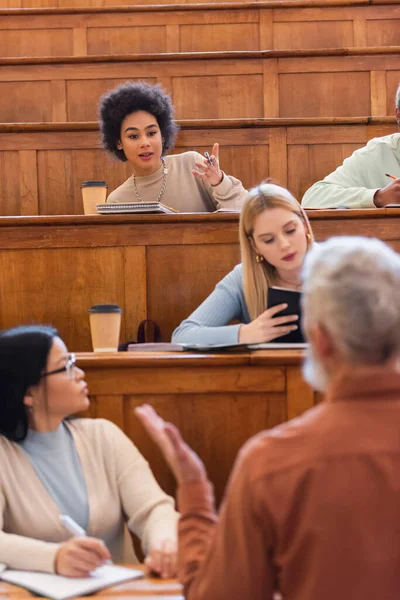 African american student talking to blurred teacher near multiethnic friends in university — Stock Photo