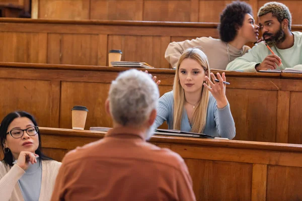 Multicultural students looking at blurred professor during lecture in university — Stock Photo