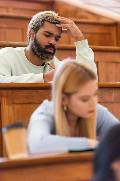 African american student sitting near blurred friends in auditorium of university — Stock Photo