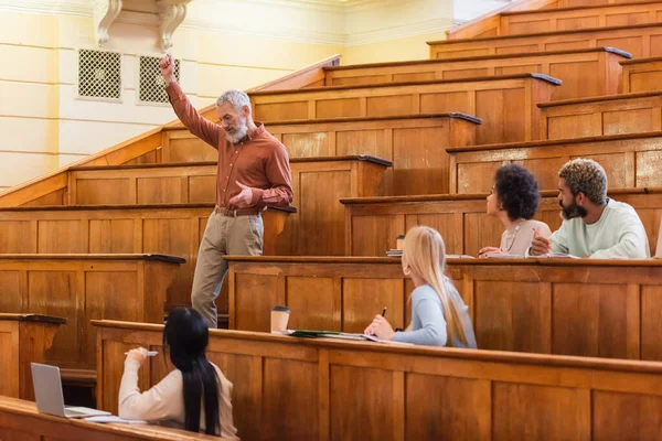 Professeur mature parlant pendant la conférence près des étudiants multiethniques à l'université — Photo de stock