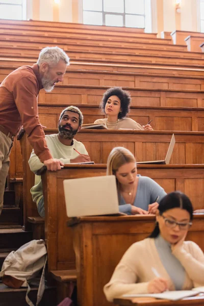 Estudantes afro-americanos olhando para o professor enquanto escreviam em cadernos na universidade — Fotografia de Stock