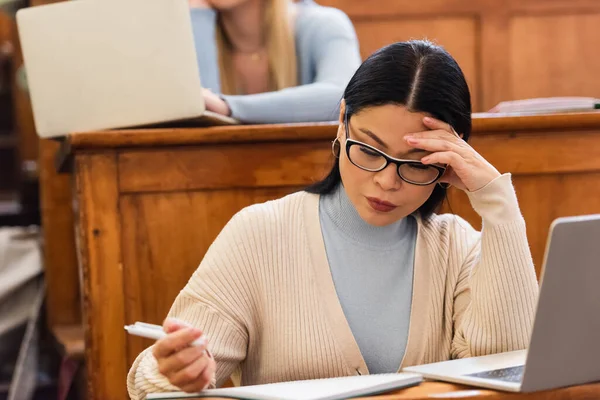 Asian student looking at notebook near laptop during lecture in university — Stock Photo