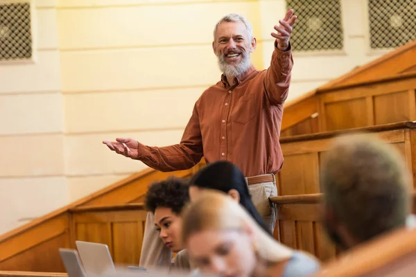 Professeur positif avec de la craie parlant à des étudiants multiethniques lors d'une conférence à l'université — Photo de stock