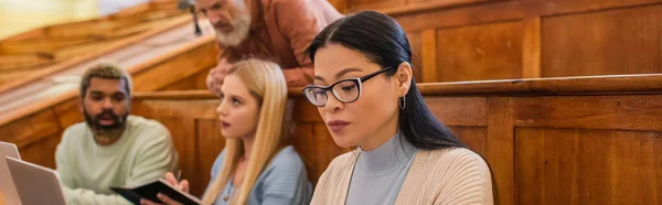 Asiático estudiante sentado cerca interracial amigos y profesor en la universidad, bandera - foto de stock