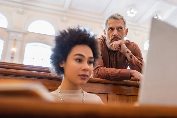 Pensive teacher near blurred african american student with laptop in university — Stock Photo