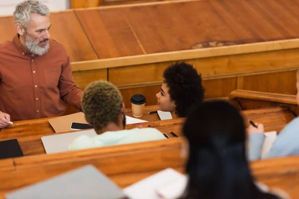 Lächelnder Lehrer mit Kreide in der Nähe afrikanisch-amerikanischer Studenten an der Universität — Stockfoto