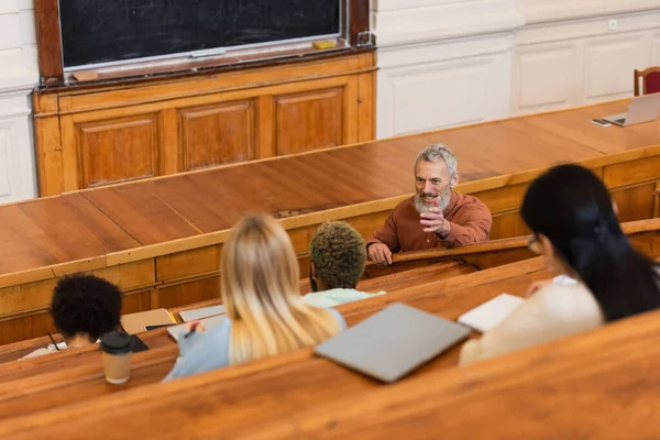 Professeur positif parlant à des étudiants interraciaux à l'audition de l'université — Photo de stock