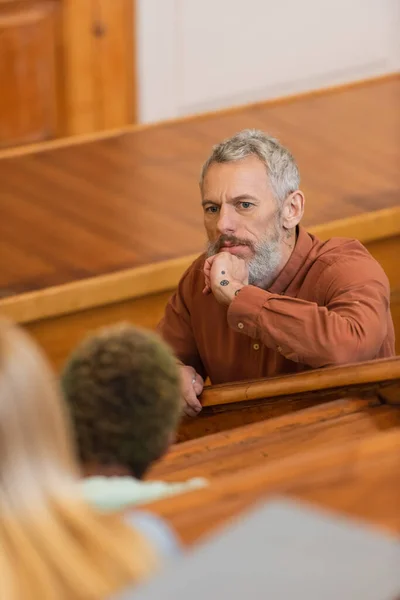 Middle aged teacher looking at blurred students in university auditorium — Stock Photo