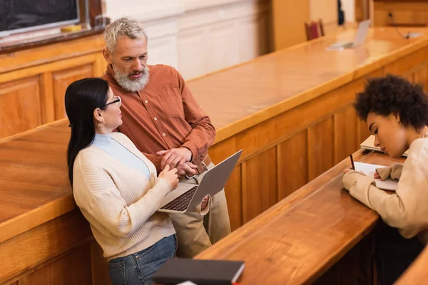 Asian student talking to mature teacher in auditorium of university — Stock Photo