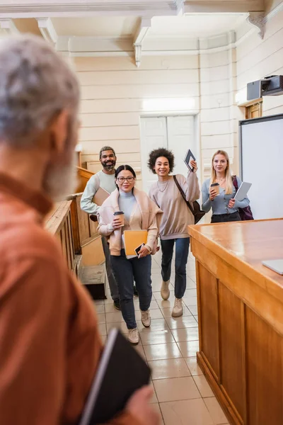 Étudiants interraciaux avec des appareils et du café pour aller regarder flou enseignant à l'université — Photo de stock