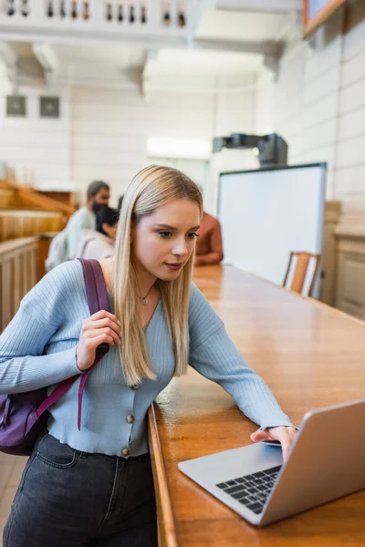 Student with backpack using laptop in university — Stock Photo