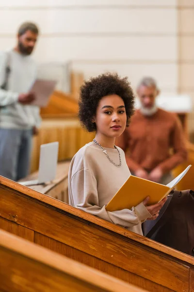 Young african american student with notebook looking at camera in university auditorium — Stock Photo