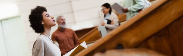 Étudiant afro-américain avec ordinateur portable regardant loin dans l'auditorium de l'université, bannière — Photo de stock