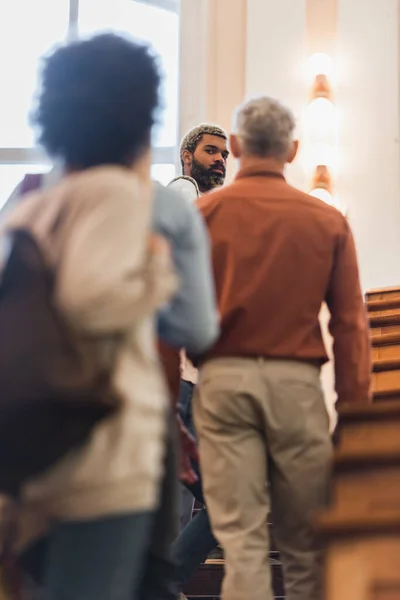 African american student looking at camera near blurred friends and teacher in university — Stock Photo