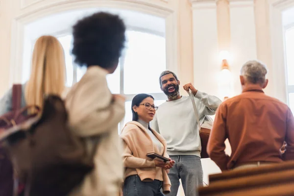 Alegre africano americano estudiante celebración mochila cerca asiático amigo y profesor en universidad - foto de stock