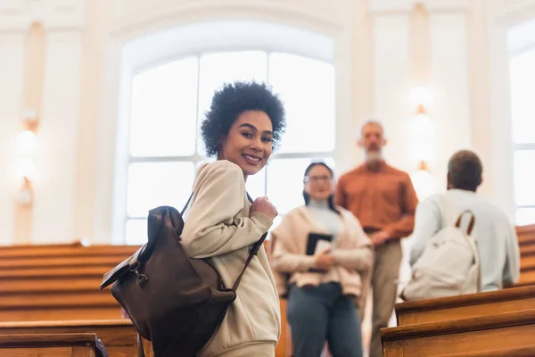 Молода афроамериканська студентка з рюкзаком посміхається перед камерою в університеті. — стокове фото
