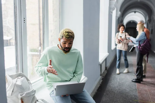 African american student using laptop near backpack in windowsill in university — Stock Photo