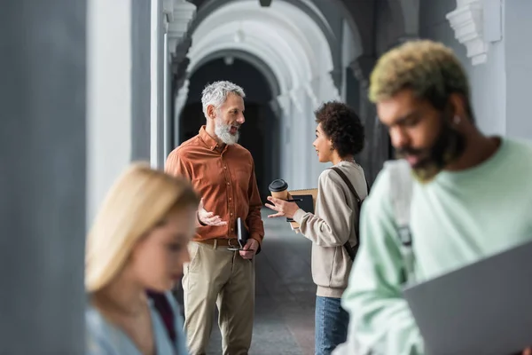 Professeur positif et étudiant afro-américain avec café pour aller parler dans le couloir universitaire — Photo de stock