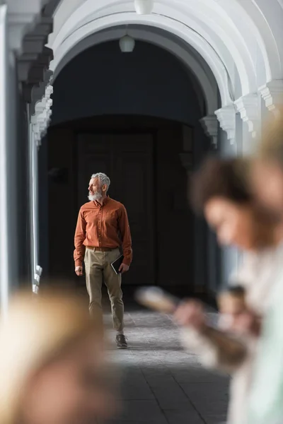 Зрелый учитель держит тетрадь в коридоре университета — стоковое фото