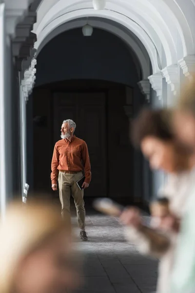 Profesora madura sosteniendo cuaderno en pasillo de universidad - foto de stock