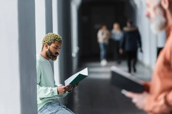 Jeune étudiant afro-américain regardant un cahier près d'un professeur flou à l'université — Photo de stock