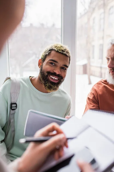 Smiling african american student looking at blurred friend near teacher in university — Stock Photo