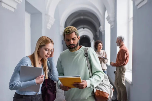 Multiethnic students holding notebooks and laptop in hall of university — Stock Photo