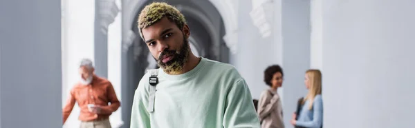 Studente afroamericano con zaino che guarda la macchina fotografica nel corridoio dell'università, banner — Foto stock