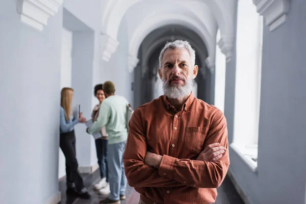 Maturo insegnante guardando la fotocamera nel corridoio dell'università — Foto stock