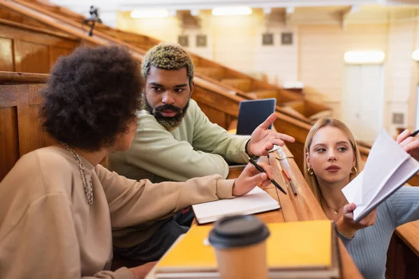 Studentin hält Notizbuch in der Nähe afrikanisch-amerikanischer Freunde und spricht in der Universität — Stockfoto