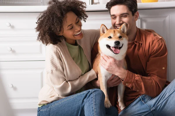 Animado casal multiético abraçando shiba inu cão na cozinha — Fotografia de Stock