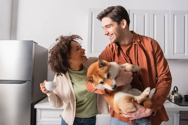 Excited interracial couple looking at each other near funny shiba inu dog — Stock Photo
