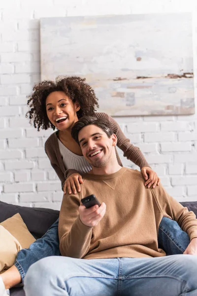 Fröhliche Afroamerikanerin umarmt Freund zu Hause mit Fernbedienung — Stockfoto